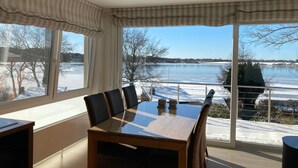 A dining area with a glass-top table, black chairs, and a view of a lake through large windows. - in Klingberg mit Seeblick by Interhome (Scharbeutz)