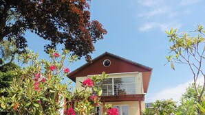 A two-story house with a balcony, surrounded by lush greenery and flowering plants. - in Klingberg mit Seeblick by Interhome (Scharbeutz)