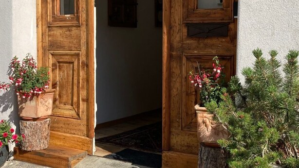 A wooden entrance with a number '12' sign, a rustic door, and potted plants. - Chesa Robbi S-chanf by Interhome (S-chanf)