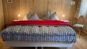 A wooden-paneled room with a bed, two bedside lamps, and a chair. - Chesa Robbi S-chanf by Interhome (S-chanf)