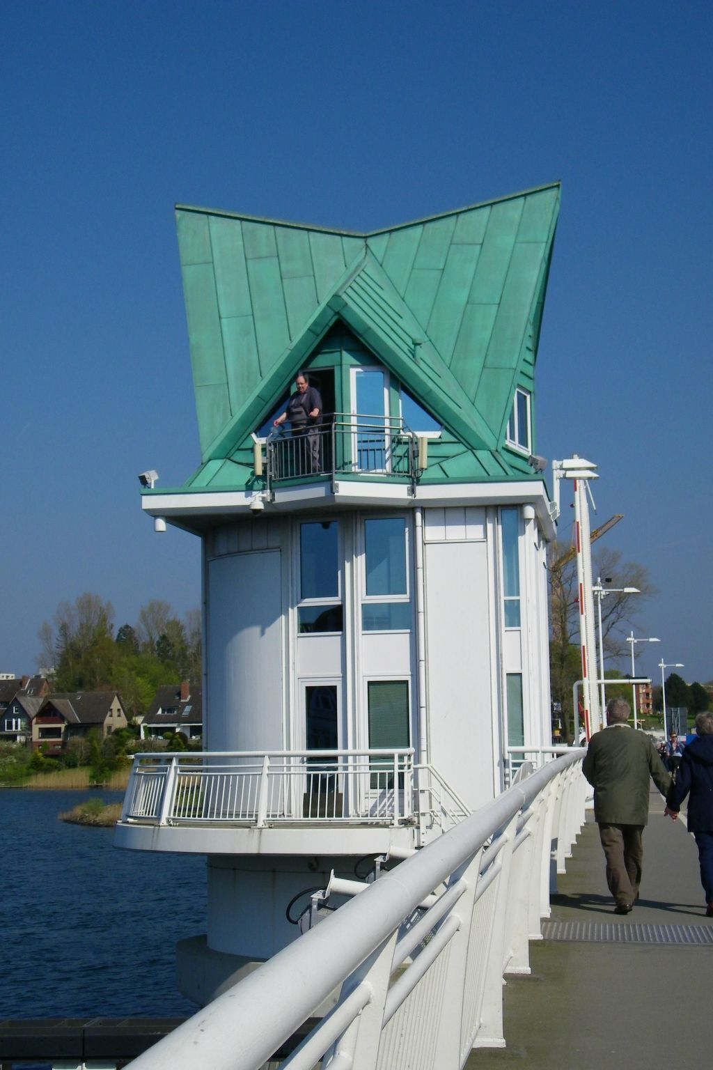 Una estructura en forma de torre amb un teulat verd, un balcó i una barana al costat d'un camí marítim.