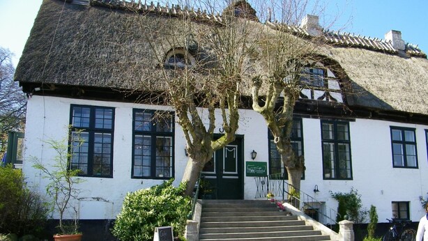 Ein traditionelles, weißes Gebäude mit einem Reetdach, einer Treppe, die zum Eingang führt, und einem Schild, das ein Café anzeigt.