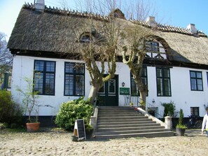 A traditional white building with a thatched roof, a staircase leading to the entrance, and a sign indicating a cafe. - Wohnung in Kappeln mit Terrasse by Interhome (Hasselberg)