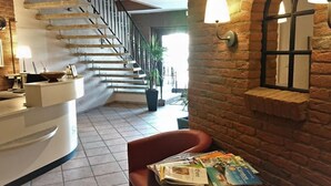 Un vestíbulo de hotel con un mostrador de recepción curvo, una escalera y una zona de estar con revistas.