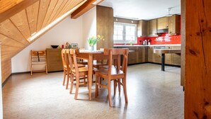 Ein Essbereich mit Holztisch und -stühlen, eine Küche mit roten Fliesen und eine geneigte Decke mit Holzbalken.