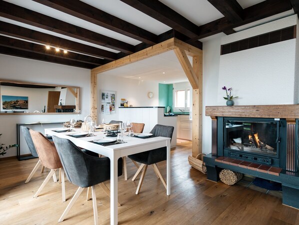 Un comedor moderno con una mesa y sillas de madera, una chimenea y una cocina al fondo.