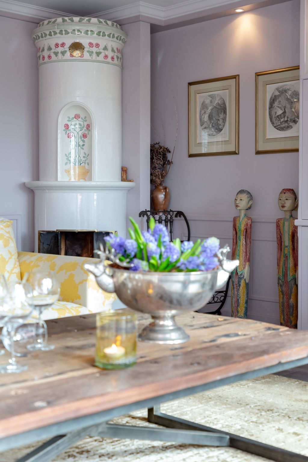 Una habitación con chimenea blanca, una mesa con un cuenco de flores plateado y dos cuadros en la pared.