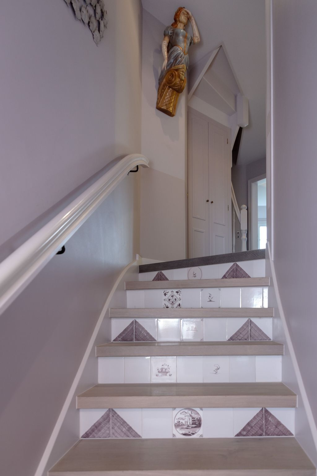 Una escalera con paredes blancas, barandilla de madera y azulejos decorativos.