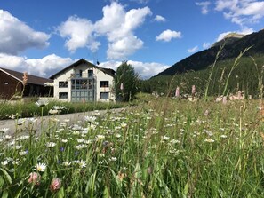 Um edifício moderno com uma grande fachada de vidro, rodeado por um campo de flores silvestres e uma montanha ao fundo.