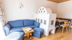 Een knus ingerichte kamer met een blauwe bank, een klein houten tafeltje en een witte constructie die op een hutje met ramen lijkt.