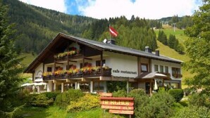 Een berghotel met een café en restaurant, omgeven door weelderige begroeiing en een vlag.
