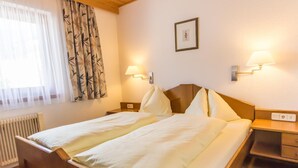 Een hotelkamer met een houten bed, twee bedlampen, een radiator en een raam met dunne gordijnen.