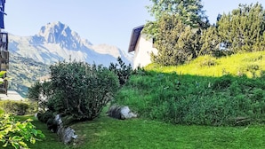 Un espace extérieur verdoyant, avec un bâtiment, des arbres et des montagnes en arrière-plan.