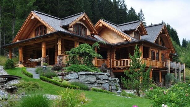 A log cabin with a stone foundation, wooden deck, and a stone retaining wall.
