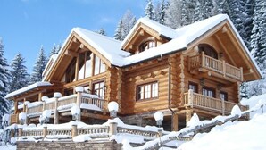 A log cabin with multiple balconies, stone foundation, and snow-covered surroundings.