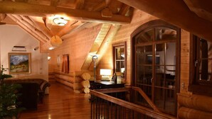 A log cabin interior with a wooden staircase, a living area with a sofa, and a dining table.