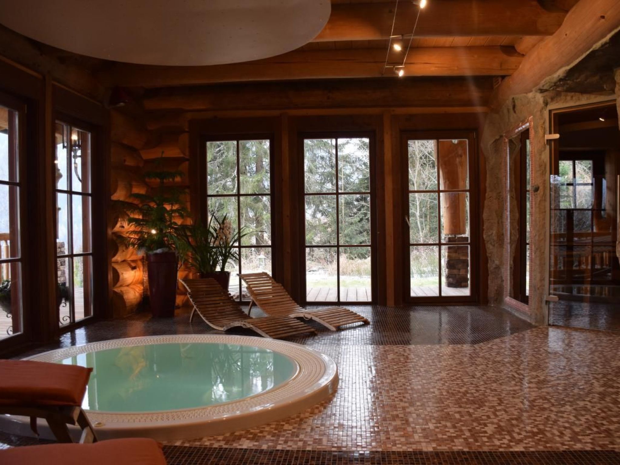 Un vaste espace intérieur abritant une piscine, doté d’un sol carrelé, de grandes fenêtres et d’un plafond en bois.