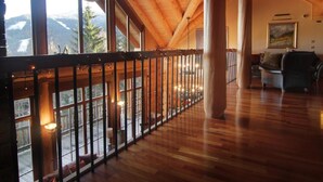 A spacious room with wooden floors, a balcony with a railing, large windows, and a couch.