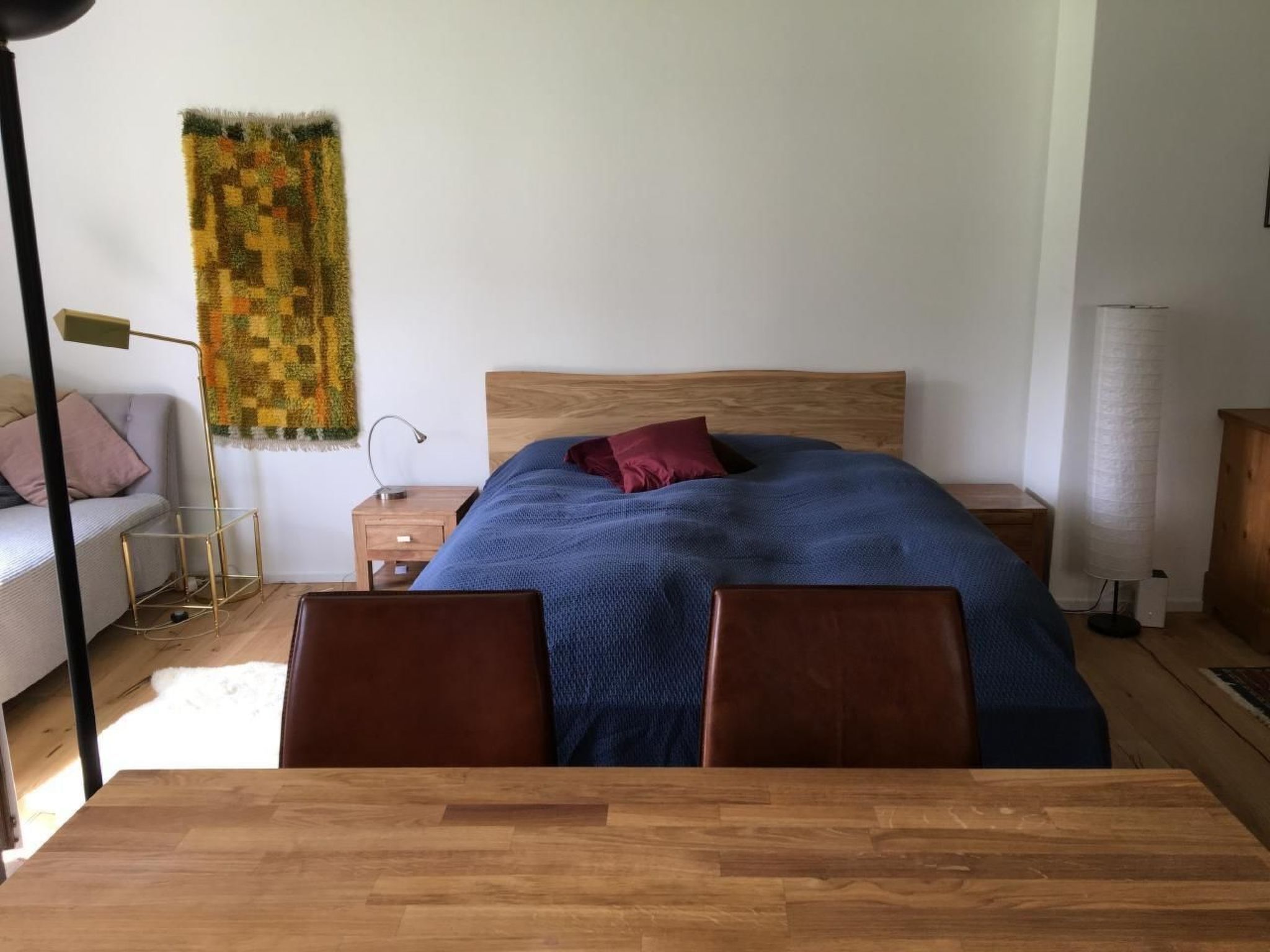 A bedroom with a wooden bed, a nightstand, a lamp, a sofa, and a table.