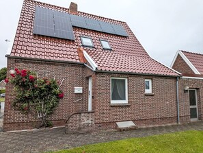 A brick building with a red-tiled roof, solar panels, a window, and a small garden with red flowers. - Seehase by Interhome (Norden)