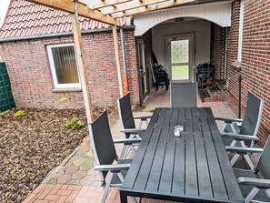 A patio with a wooden table and chairs, a brick wall, and a covered area with a door. - Seehase by Interhome (Norden)