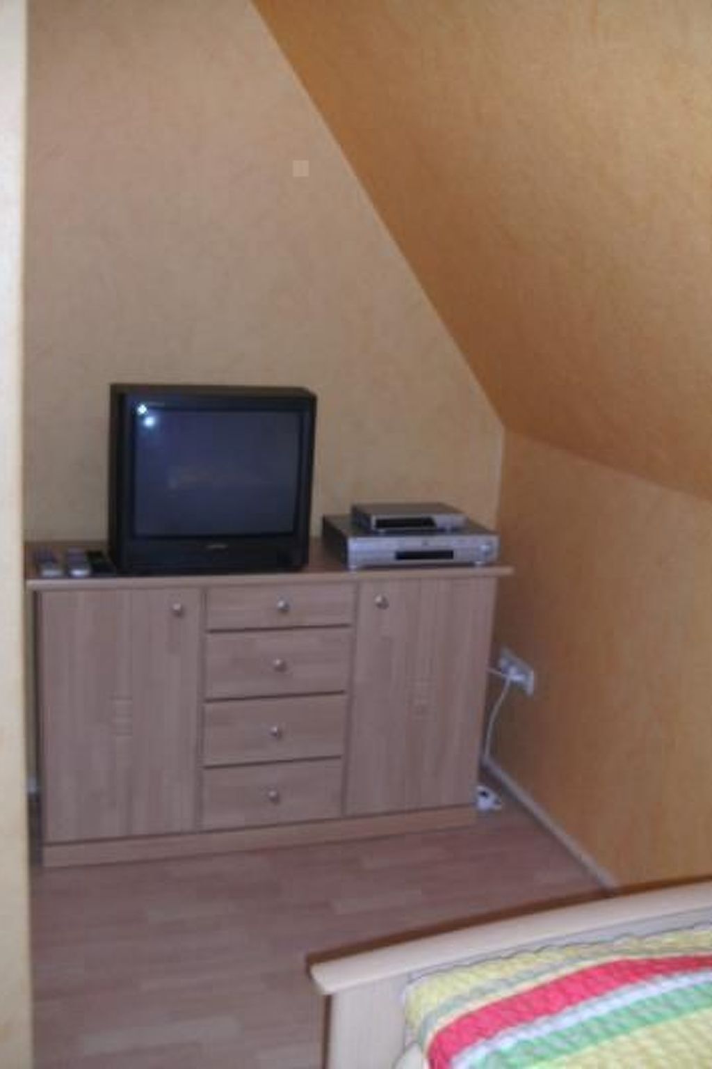 A bedroom with a bed, a television on a wooden cabinet, and a small shelf with a DVD player.
