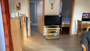 Ein gemütlicher Wohnbereich mit Fernseher auf einem Schrank, einem Holzschrank und einem Bett im Hintergrund.