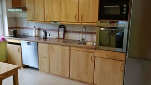 A kitchen with wooden cabinets, a stainless steel sink, a dishwasher, a microwave, and an oven. - Landblick by Interhome (Friederikensiel)