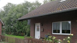 A brick house with a white door, a small porch, and a wooden fence. - Landblick by Interhome (Friederikensiel)