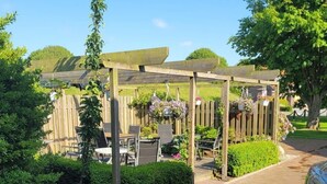 A brick pathway leading to a wooden pergola with hanging flower baskets. - Landskron by Interhome (Friederikensiel)