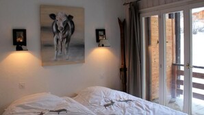 Quarto com duas camas, um quadro de uma vaca e porta de vidro que se abre para uma varanda.