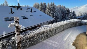 Um edifício coberto de neve com telhado inclinado, rodeado por árvores carregadas de neve e céu claro.