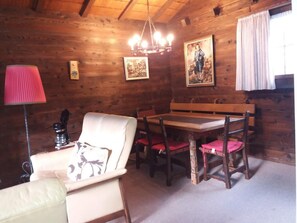 A cozy wooden cabin interior with a dining table, chairs, a sofa, and a lamp. - Chalet Holzwurm by Interhome (Oberried-Ebligen)
