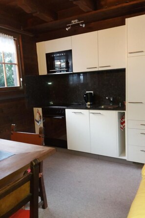 A kitchen with white cabinets, a black countertop, and a stove. - Chalet Holzwurm by Interhome (Oberried-Ebligen)