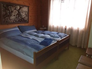 A wooden room with a bed, a nightstand, a painting on the wall, and a window with curtains. - Chalet Holzwurm by Interhome (Oberried-Ebligen)
