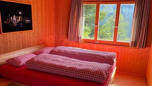 Ein Zimmer mit Holzboden, einem Bett, einem Fenster mit Vorhängen und einem Bild an der Wand.