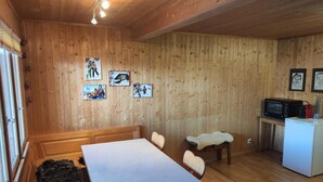 Ein gemütliches Holzhaus-Interieur mit Esstisch, Stühlen, einer kleinen Küchenzeile mit Mikrowelle und gerahmten Bildern an den Wänden.