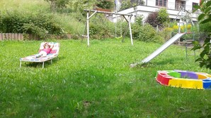 En græsplæne med gyngestativ, rutsjebane og en farverig lejemåtte.