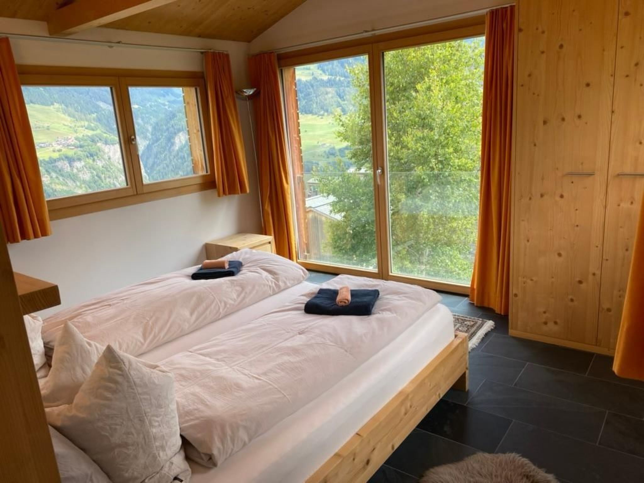 Un dormitorio con dos camas, ventanas amplias, paredes de madera y vista a zonas verdes.