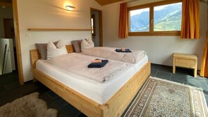 Cama doble con cabecera de madera, mesita de noche, alfombra y ventana con cortinas.