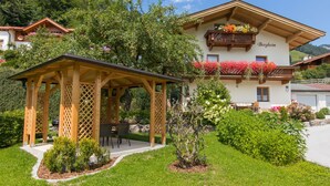 A chalet with a wooden pergola, a dining area, and a garden with various plants and flowers. - "Idylle by Interhome (Walchsee)
