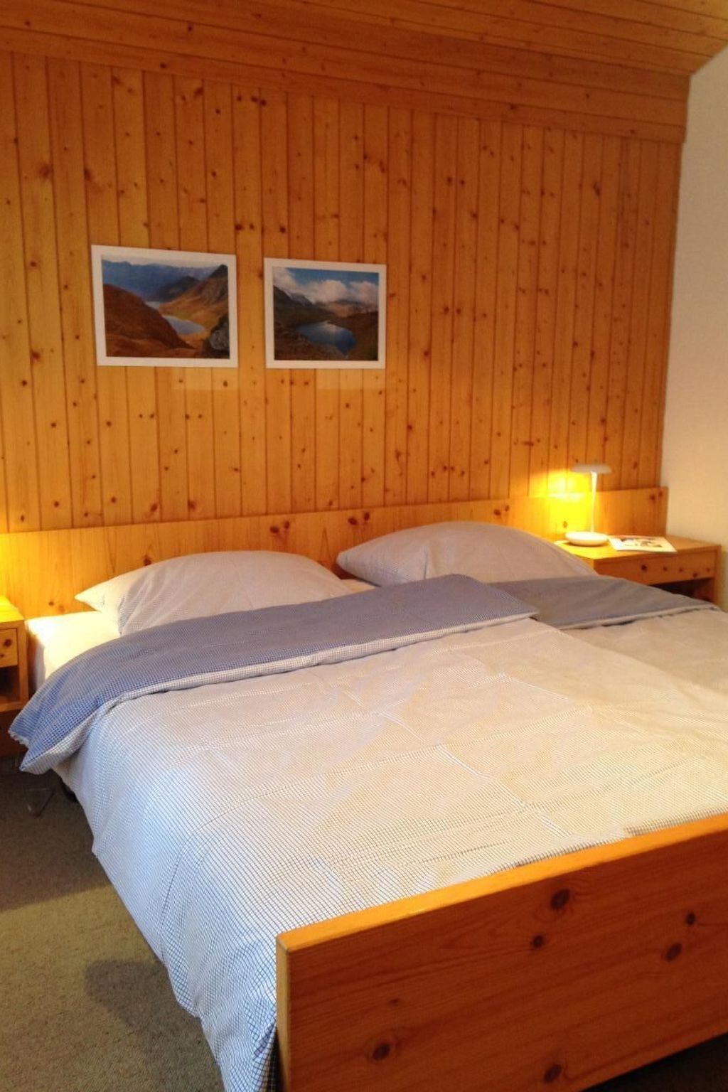 A wooden-paneled room with a bed, two nightstands, and two framed pictures on the wall.