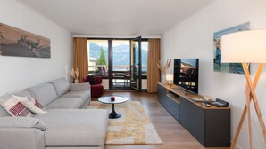En moderne stue med en grå sofa, et sofabord og et fjernsyn på et stativ.