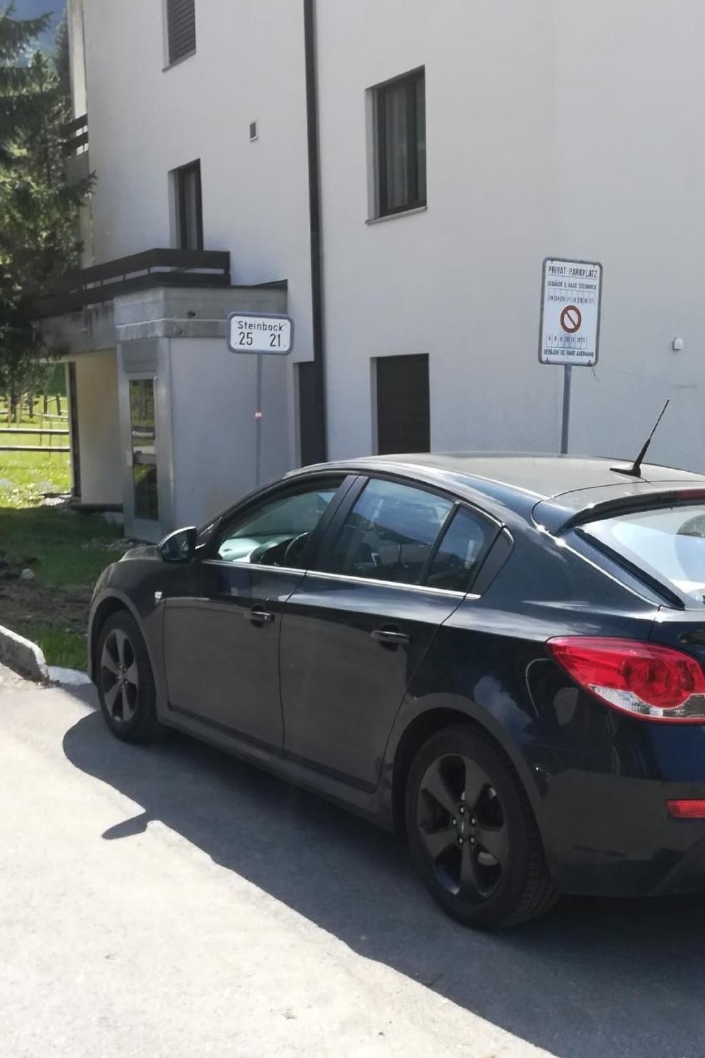 Un coche oscuro estacionado frente a un edificio con un letrero que indica 'Steinbeck 25 21'.