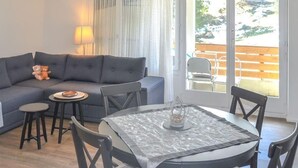 Un salon avec un canapé gris, une table ronde entourée de chaises, une petite table ronde et une lampe.