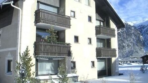A multi-story building with balconies, a stone facade, and a mountainous backdrop. - Chesa Arettas by Interhome (Bever)
