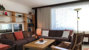 A modern living room with a sofa set, a coffee table, a bookshelf, and a large window with curtains. - Chesa Arettas by Interhome (Bever)