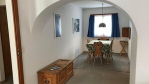 Een eetgedeelte met een tafel, stoelen, een houten bank en een raam met blauwe gordijnen.