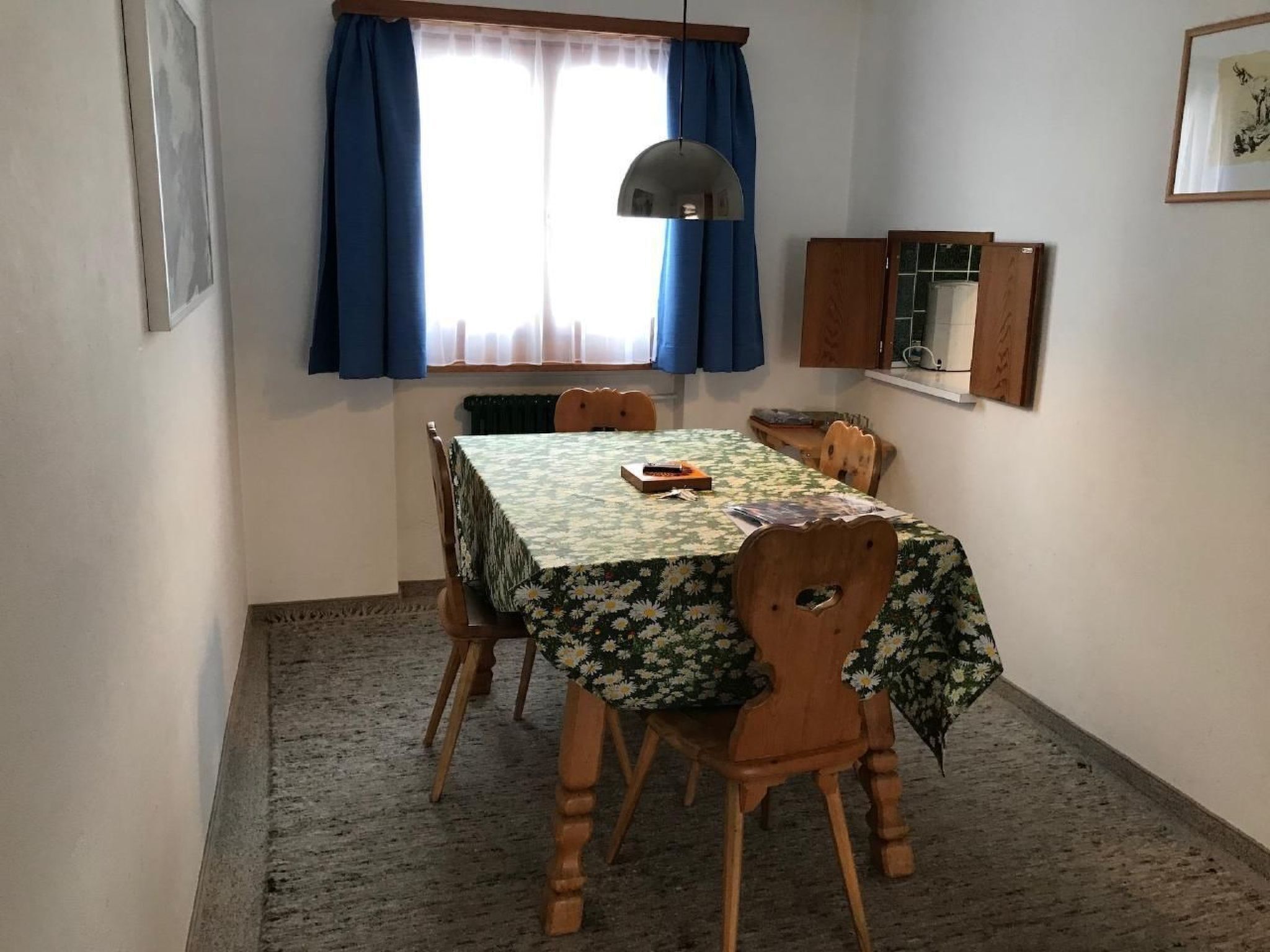 Een eethoek met een tafel, overdekt met een bloemendecoreerde tafelkleed, omringd door houten stoelen.
