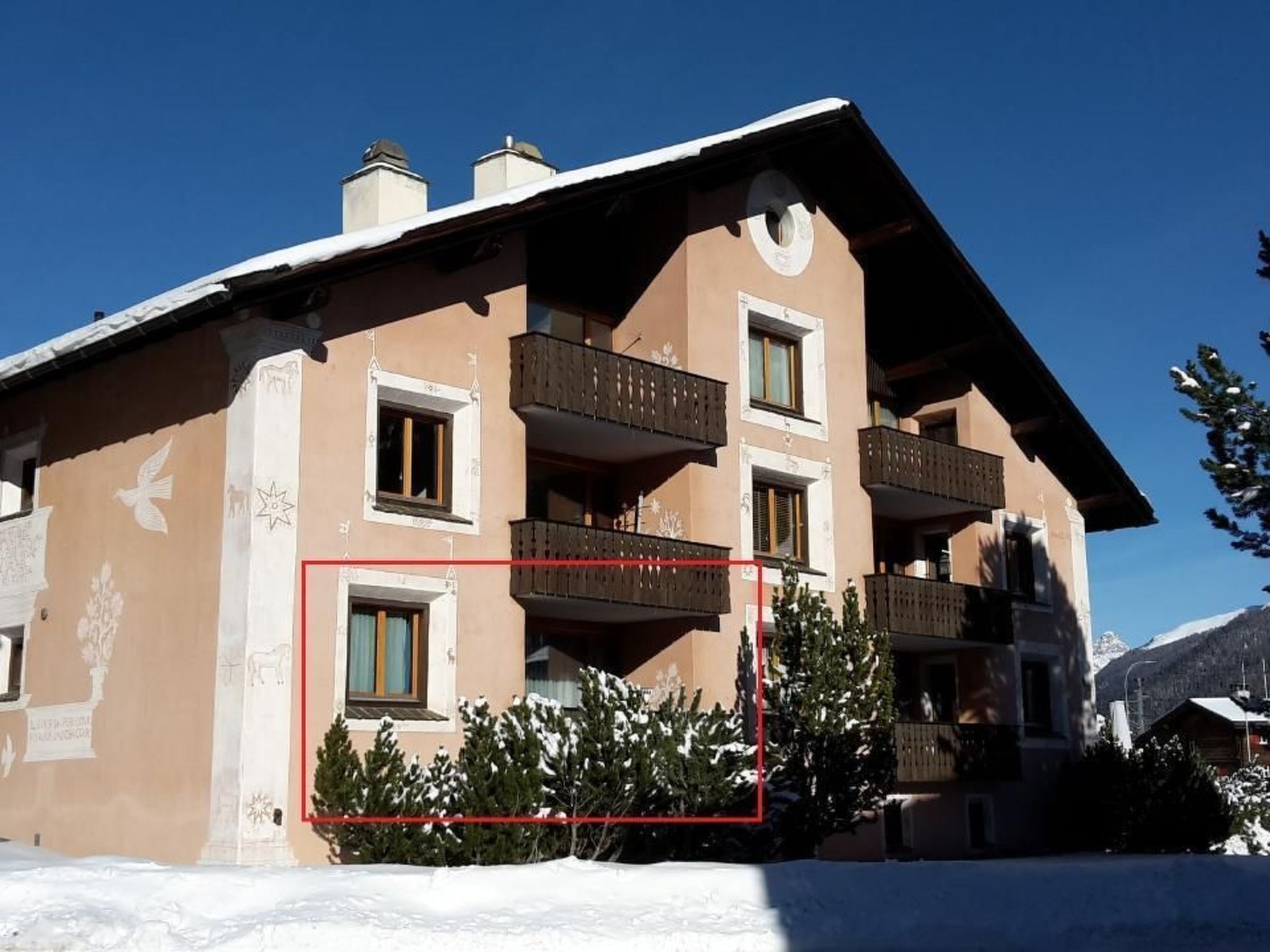 Un edificio de varios pisos con balcones, suelo cubierto de nieve y un cielo azul despejado.